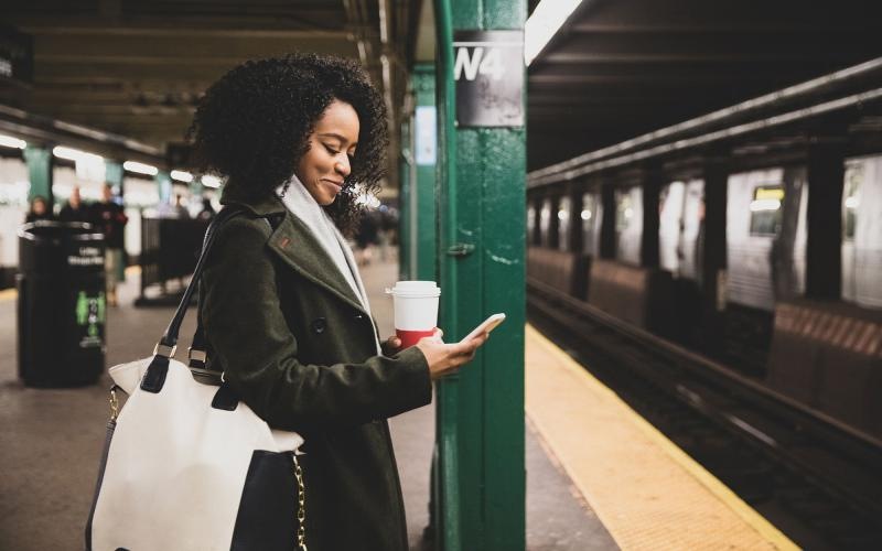 Find your perfect fit at The Sagamore woman with a cup of coffee texts on subway station platform